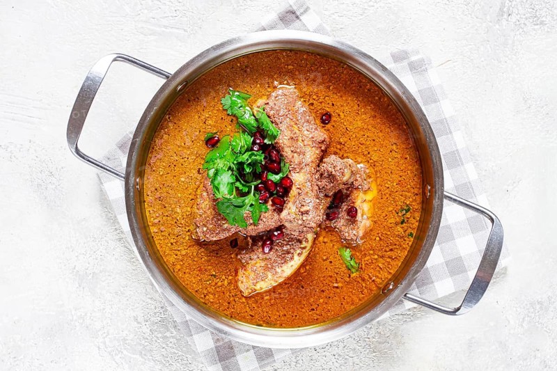 Fesenjan, an Iranian dish, stewed chicken, in a nut-pomegranate sauce, in a saucepan, light background, homemade, no people
