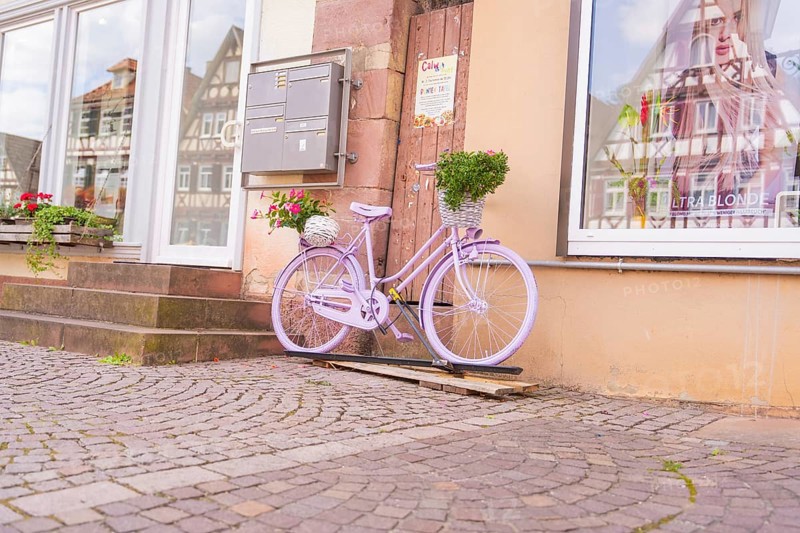 A purple bicycle with a basket of flowers in front of a building with half-timbered houses, small town of Perle Calw, Black Forest, Germany