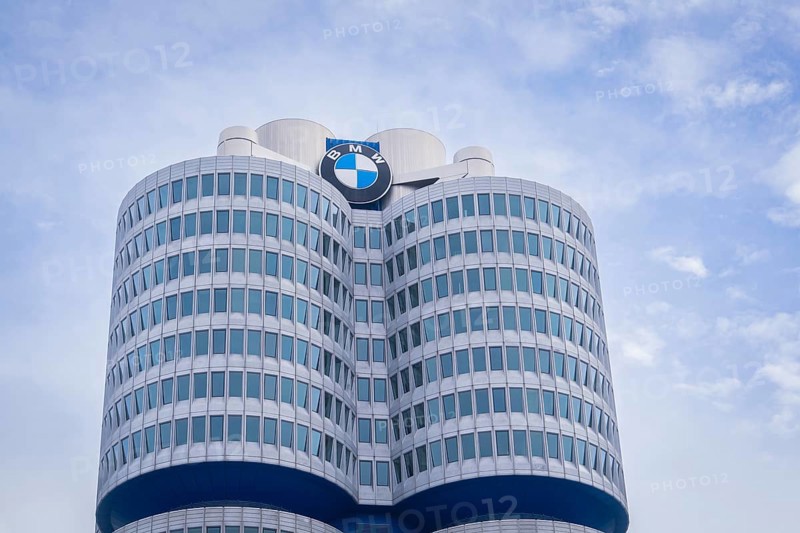 High-rise building with round glass facades and prominent logo against a slightly cloudy sky, BMW Welt, Munich, Germany