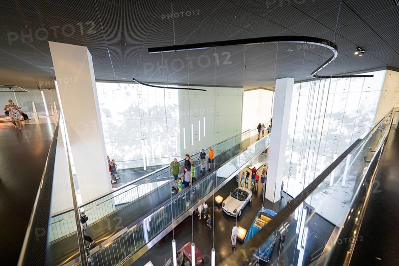 Modern interior with group of visitors and exhibited vehicles under dynamic light installations, BMW Welt, Munich, Germany