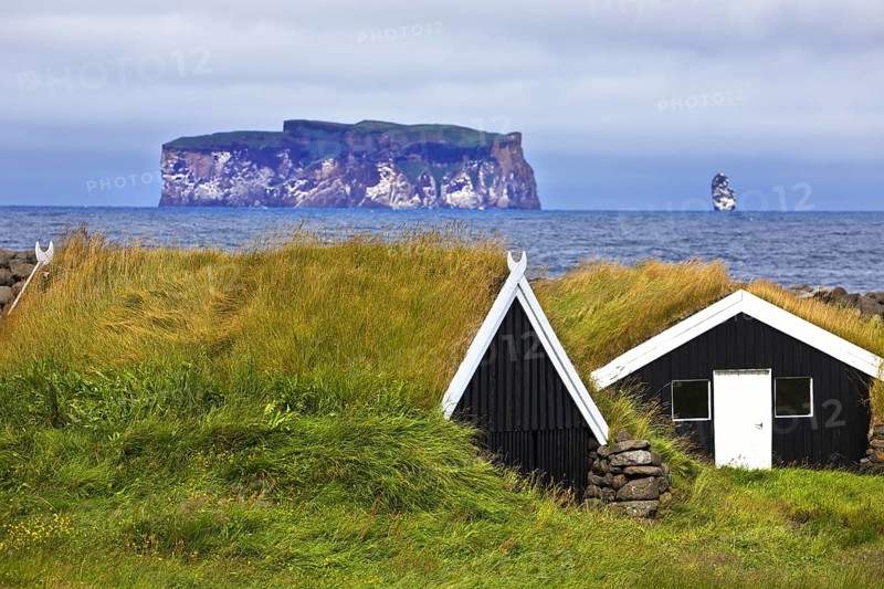 Traditional wooden huts with grass roofs in Reykjadiskur with the island of Drangey in Skagafjördur, Norurland vestra, Iceland