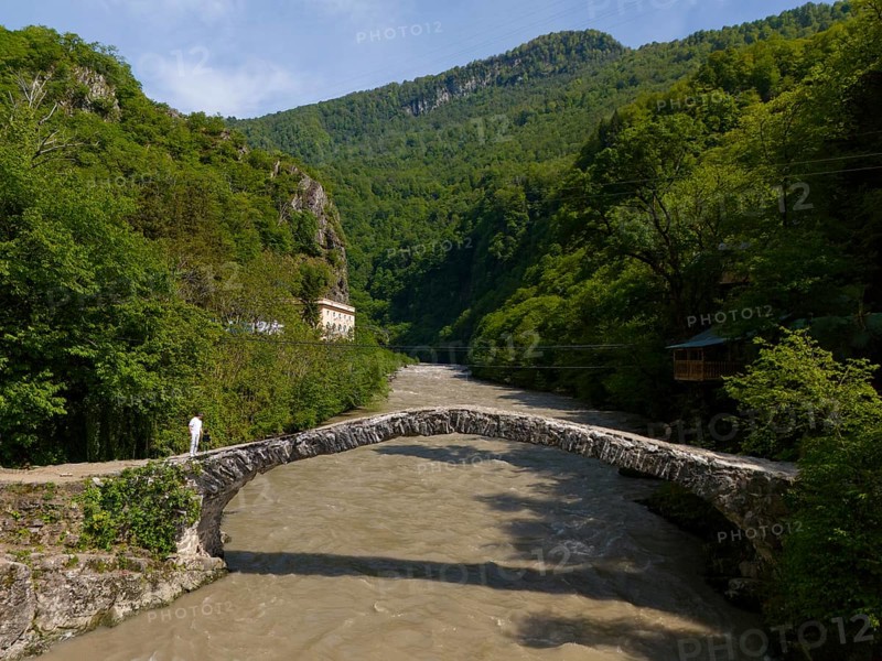 Person crossing a stone bridge over a river, surrounded by green hills and lush forest, aerial view, stone arch bridge Makhuntseti, Adjaristskali River, Adjara Autonomous Republic, Adjara, Adjara, Lesser Caucasus, Georgia