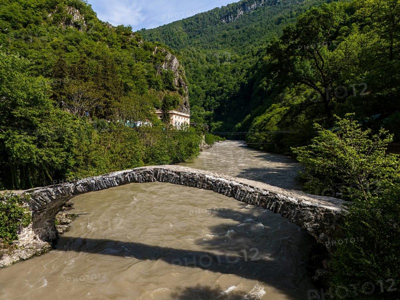 Old stone bridge over a river against a backdrop of green hills and dense forests, aerial view, stone arch bridge Makhuntseti, Adjaristskali River, Adjara Autonomous Republic, Adjara, Adjara, Lesser Caucasus, Georgia