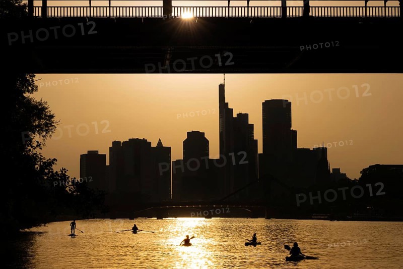 The evening sun stands over the Frankfurt banking skyline while paddlers and rowers navigate the Main, Frankfurt am Main, Hesse, Germany