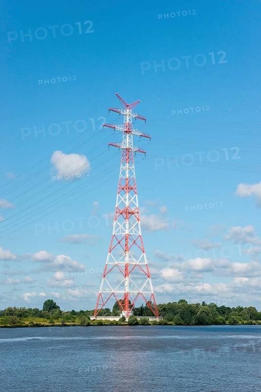 An extremely high electricity electricity electricity pylon, marked white and red, stands on the banks of the Elbe, river bank, Elbe crossing 2, 227 m high, highest overhead line pylon in Europe, surrounded by green landscape with trees and meadows under a blue sky, high-voltage pylon, overhead line pylon, overhead line, colour marking, safety, aviation safety, technology, structure, near Hollern-Twielenfleth, Lühe, Altes Land, Lower Saxony, Germany