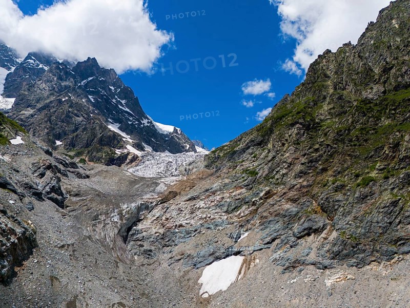 Rocky landscape with a glacier under a blue sky, flanked by mountains. Clouds drift over the alpine valley, aerial view, Chalaadi glacier, Mestia, Svaneti, Caucasus, Georgia