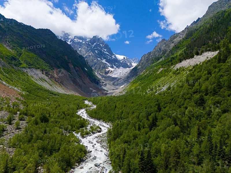 Picturesque mountain landscape with river in the foreground, lush forests and snow-capped peaks under a blue sky, aerial view, Chalaadi glacier, Mestia, Svaneti, Caucasus, Georgia