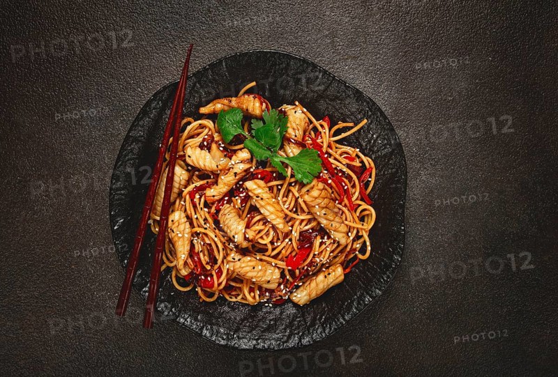 Udon noodles, with squid and vegetables, on a black plate, homemade, no people