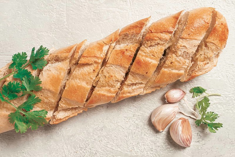 Garlic bread, baguette with garlic butter and herbs, on a light table, top view
