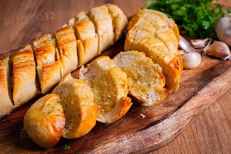 Garlic bread, baguette with garlic butter and herbs, on a wooden board, with herbs and garlic cloves