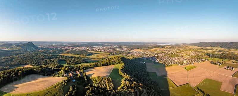 Luftbild, Panorama von einer vulkanisch geprägten Landschaft im Abendlicht, im Vordergrund der Phonolithkegel Rosenegg, am Horizont die Hegauberge mit dem Hohentwiel und der Stadt Singen und der angrenzenden Gemeinde Rielasingen-Worblingen, Hegau, Landkreis Konstanz, Baden-Württemberg, Deutschland