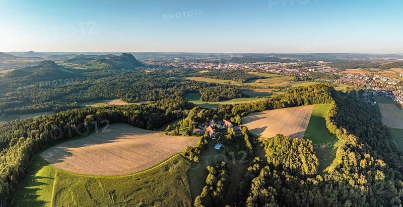 Luftbild, Panorama von einer vulkanisch geprägten Landschaft im Abendlicht, im Vordergrund der Phonolithkegel Rosenegg, am Horizont die Hegauberge mit dem Hohentwiel und der Stadt Singen mit der angrenzenden Gemeinde Rielasingen-Worblingen, Hegau, Landkreis Konstanz, Baden-Württemberg, Deutschland