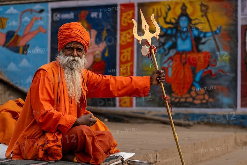 Indian sadhu holding trident, with image of Shiva in the background, Bangali Tola, Varanasi, Uttar Pradesh, India