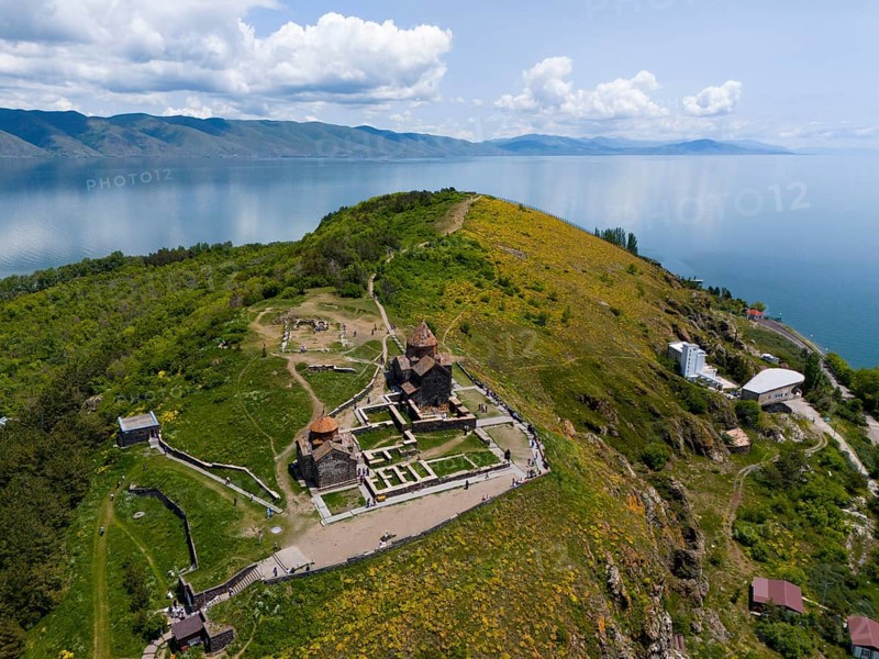 Panorama of a monastery on a green hill with a view of a lake and mountains under a cloudy sky, aerial view, Sevanavank Monastery, Sevan Monastery, Gegharkunik Province, Armenia