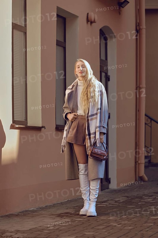 The young woman exudes confidence in a chic autumn outfit featuring a brown skirt and white knee-high boots