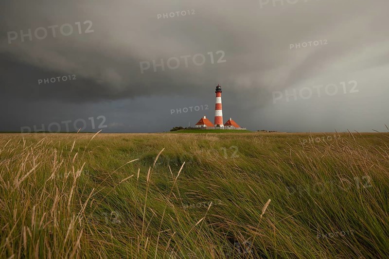 Illuminated Westerheversand lighthouse on the North Sea under dark storm clouds