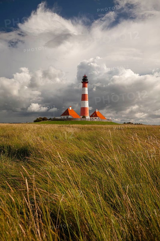 Illuminated Westerheversand lighthouse on the North Sea under dark storm clouds