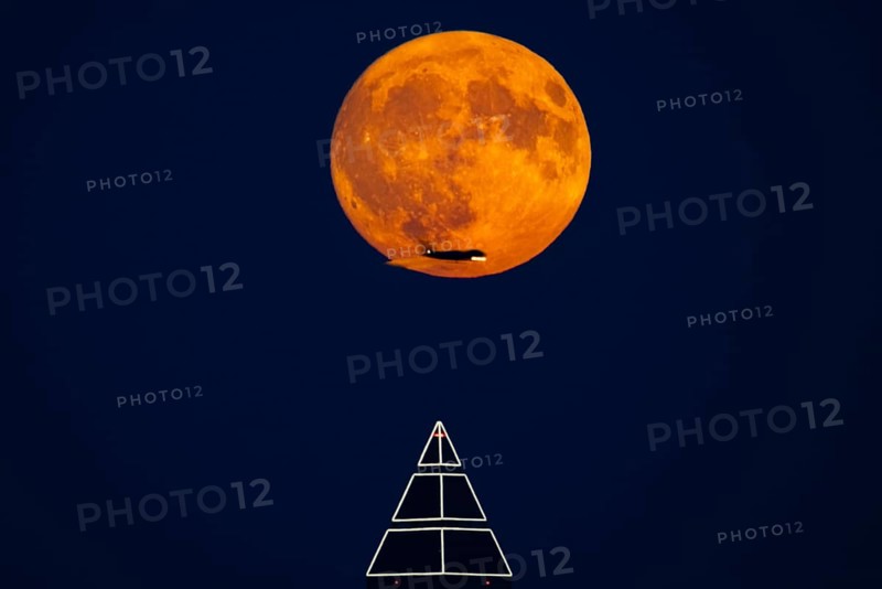 The full moon passes over the top of the Messeturm in Frankfurt am Main, while the silhouette of an aeroplane appears in front of it, Frankfurt am Main, Hesse, Germany