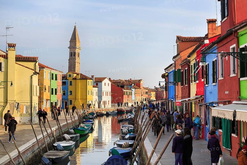 Strollers along the canal, typical street scene in winter, campanile of the church of San Martino, colourful facades of the fishermen's houses in Burano, island in the lagoon of Venice, Italy