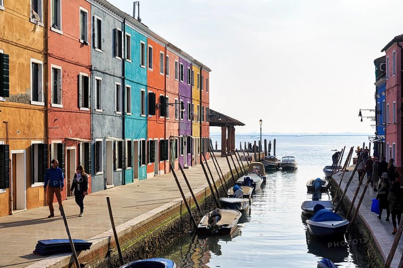 Strollers along the canal, typical street scene in winter, colourful facades of fishermen's houses in Burano, haze, island in the lagoon of Venice, Italy