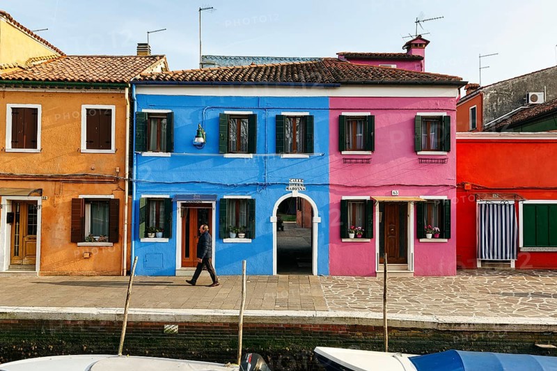 Lone walker on the canal, typical street scene in winter, colourful facades in Burano, island in the lagoon of Venice, Italy