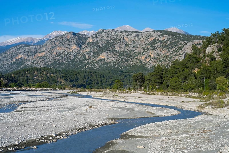 A calm river flows through a wide gravel bed, framed by forested mountains, Dargaz River near Saklikent, Saklikent, Antalya Province, Turkey