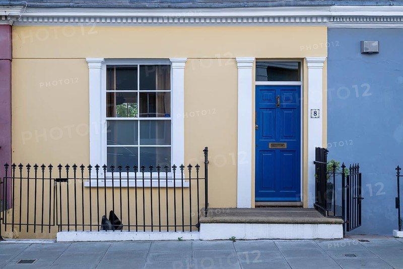 Colourful townhouse with blue door and yellow façade, surrounded by black fence, Kensington, London, England, United Kingdom