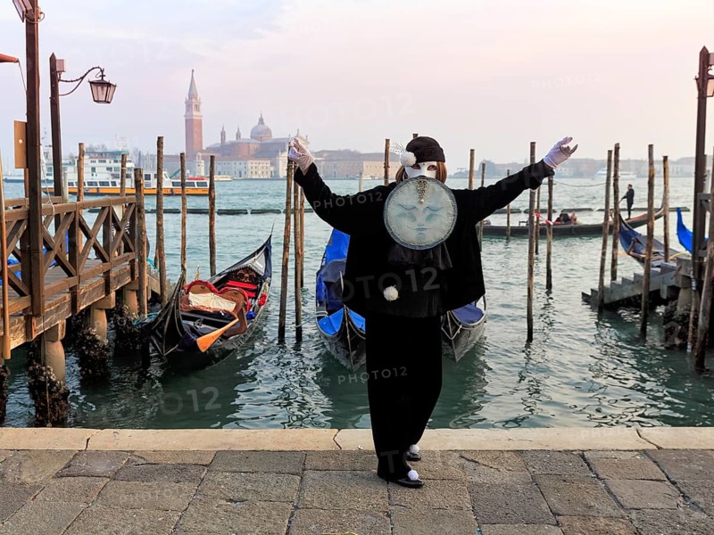 Person with black costume and mask, full moon mask, boat dock at St Mark's Square, behind the church of San Giorgio Maggiore, Carnival in Venice, Italy