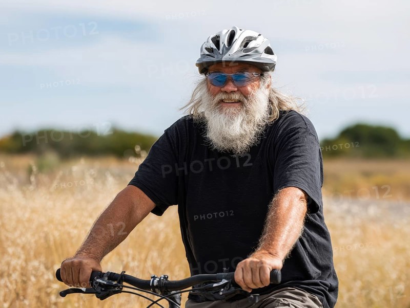 A man, senior citizen with a bicycle helmet rides on a bicycle and smiles friendly into the camera, AI generated, AI generated