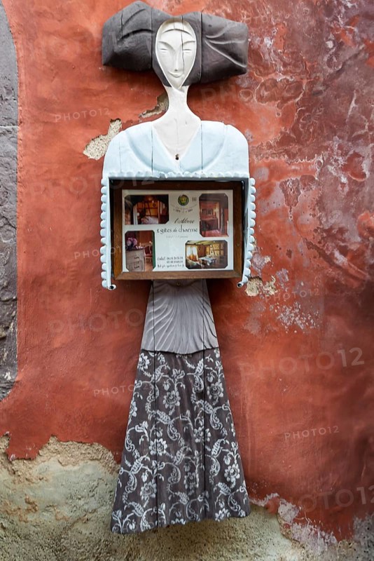 Abstract sculpture of a woman on a rust-red plastered wall. Figure holding a box with photos, vintage style, Eguisheim, Alsace, France