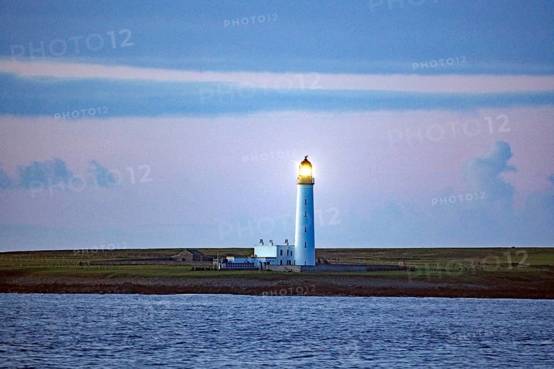 Lighthouse on the coast at dusk with blue sky in the background, crossing between Orkney and Shetland Islands, Scotland, Great Britain