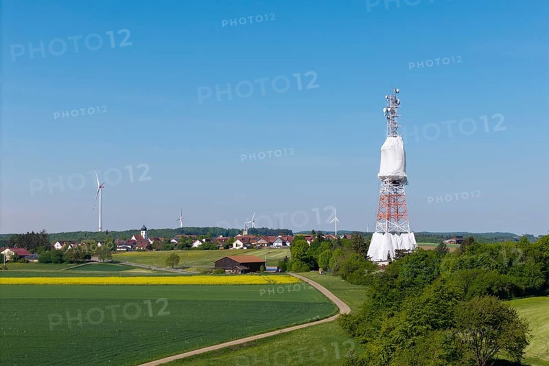 A transmission tower and wind turbines near a village under a blue sky, radio tower being renovated, near Hohenstadt, Swabian Alb, Baden-Württemberg, Germany