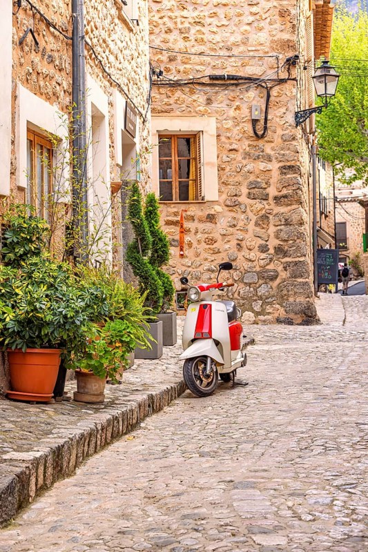 Scooter standing outside a house on the city street with lush green plants in pots on the pavement in an idyllic spanish village, Sóller, Mallorca, Spain
