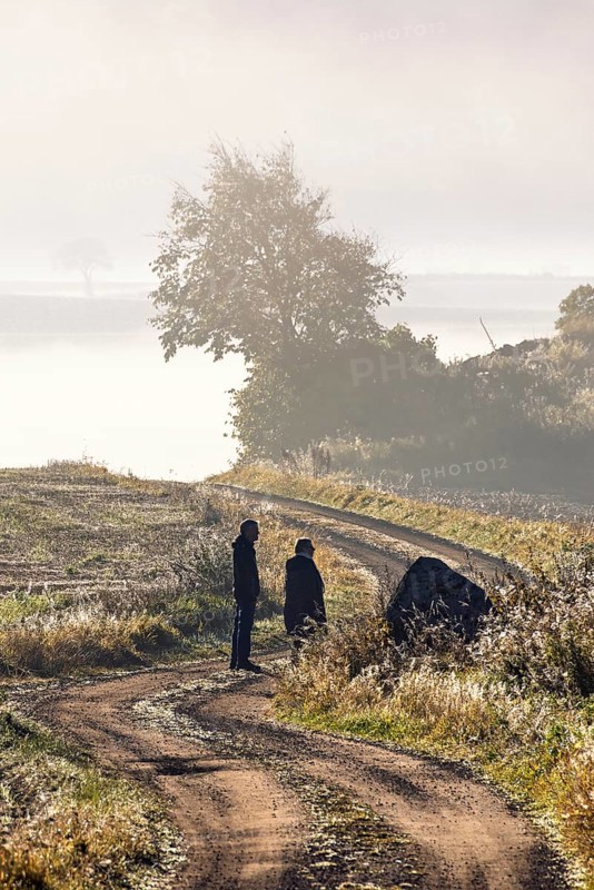 Two people walking on a winding gravel road in the countryside on a foggy autumn day