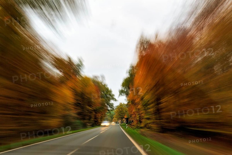 Country road through autumn forest, autumn leaves, oncoming traffic, light traces, cloudy weather, zoom effect, motion blur, Solling-Vogler nature park Park, Lower Saxony, Germany