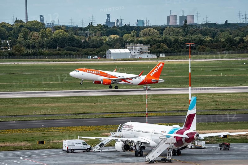 Düsseldorf Airport, Eurowings Airbus aircraft on the apron, EasyJet Airbus A320-200 taking off, in the background the HKM steelworks in Duisburg, North Rhine-Westphalia, Germany