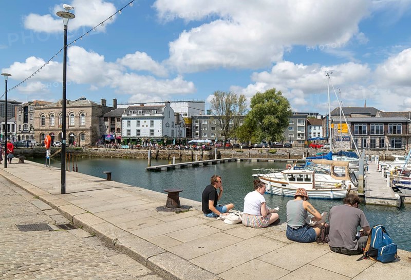 People sitting on quayside of marina harbour, The Barbican, Plymouth, Devon, England, UK