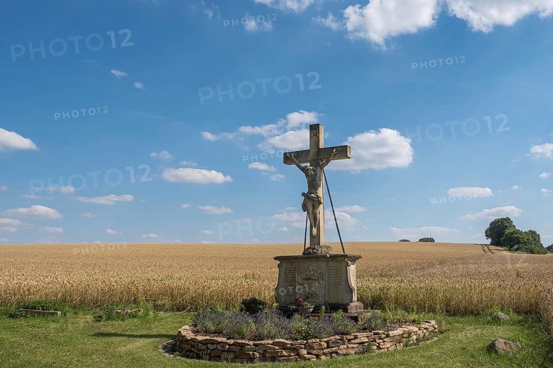 A crucifix, field cross stands in front of a grain field under a blue sky with clouds, Münsterland, North Rhine-Westphalia, Germany