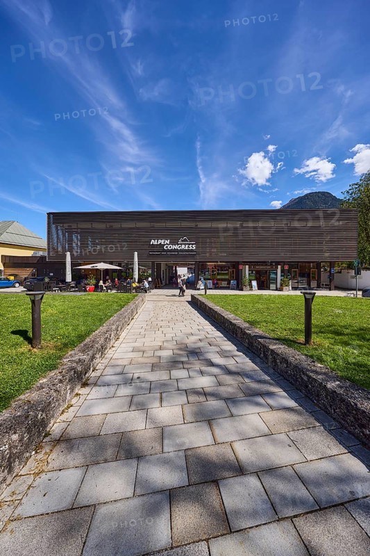 AlpenCongress Berchtesgaden, congress hall, modern architecture, building, outdoor area of a restaurant with parasols, lawn, footpath, paving slabs, lamp, blue sky, cumulus clouds, cirrostratus clouds, Maximilianstraße, Berchtesgaden, Upper Bavaria, district of Berchtesgadener Land, Bavaria, Germany