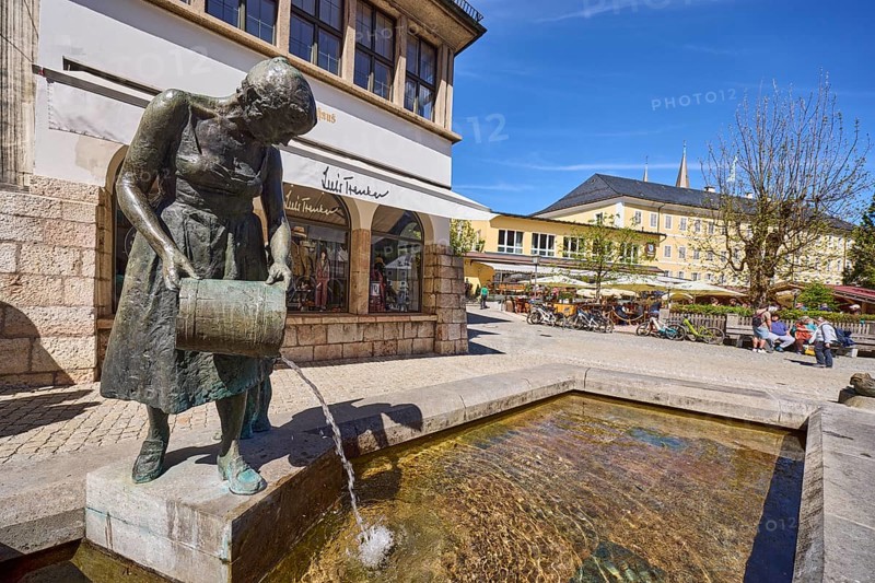 Mother-child fountain, fountain with bronze sculptures, sculptor Fritz Schelle, square, pedestrian zone, outdoor area of a restaurant with parasols, visitors as secondary motif, general architecture, fashion shop, retail trade, blue sky, cirrostratus clouds, market square, Metzgerstraße, Berchtesgaden, Upper Bavaria, district of Berchtesgadener Land, Bavaria, Germany