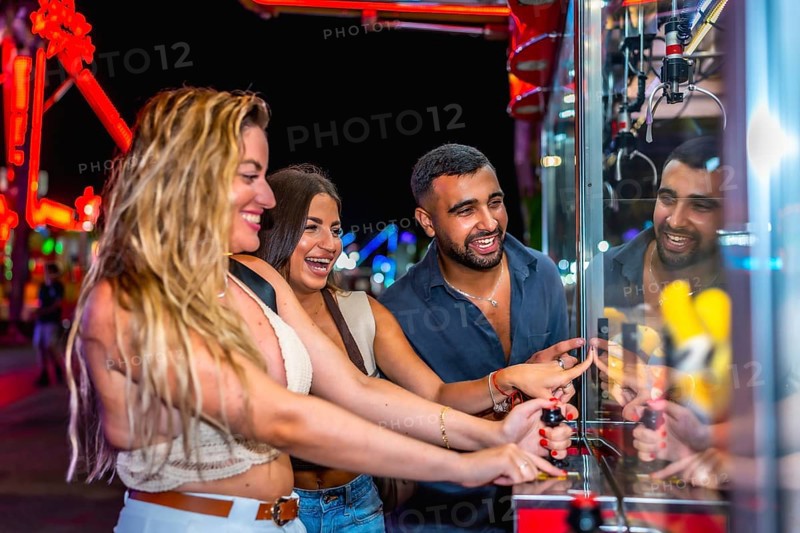 Happy friends enjoying a night out at amusement park, playing skill crane game and trying to win a prize