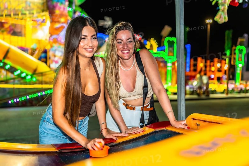 Two friends enjoying a game of air hockey at a brightly lit amusement park, adding excitement to their night out