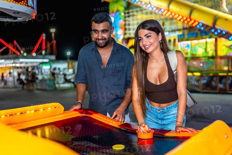 Happy young couple enjoying a lively night out, playing air hockey together at a colorful amusement park filled with excitement and joy