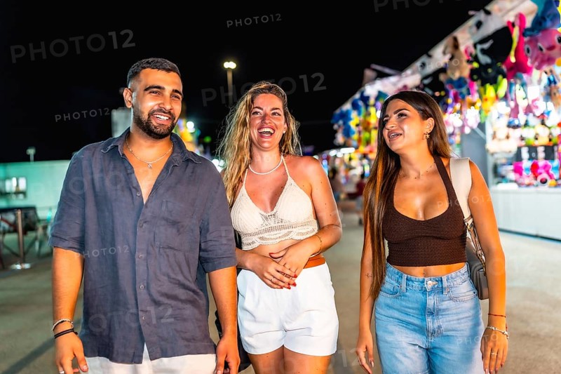 Three friends are enjoying their time together, strolling through a vibrant amusement park at night