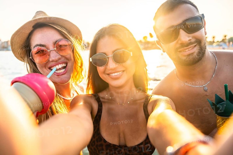 Group of cheerful multi ethnic friends taking selfie at beach party, enjoying refreshing drinks during sunset