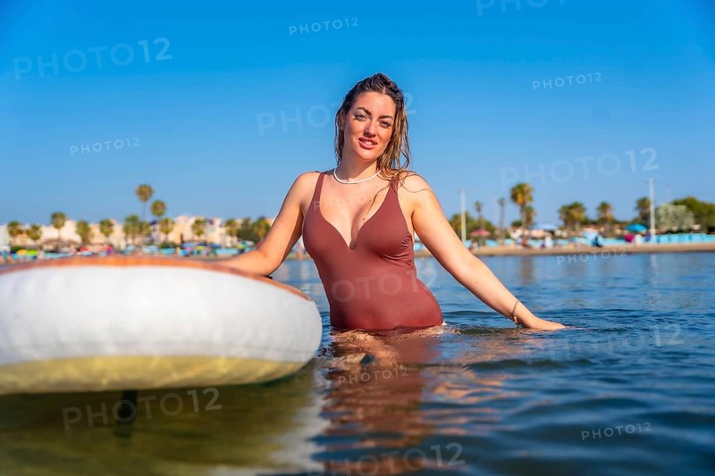 Young woman enjoying paddle surfing in the calm sea on a sunny summer day, embracing the tranquility and watersports lifestyle