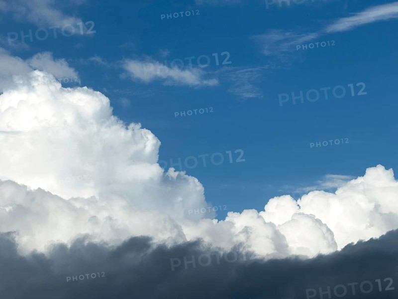 At the bottom of the picture grey nimbostratus clouds, above white cumulus cumulus clouds in front of a blue sky, International