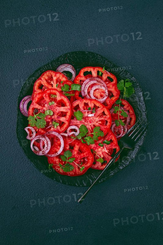 Freshly sliced tomatoes and red onions, garnished with herbs, on a black plate, summer salad, no people
