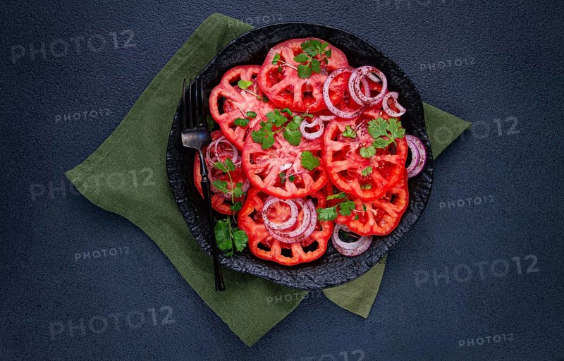 Freshly sliced tomatoes and red onions, garnished with herbs, on a black plate, summer salad, no people