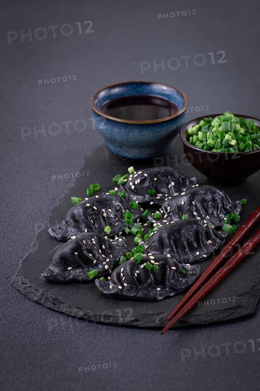 Japanese gyoza dumplings, made of black dough, black gyoza, with green onions and sauce, on a plate, close-up